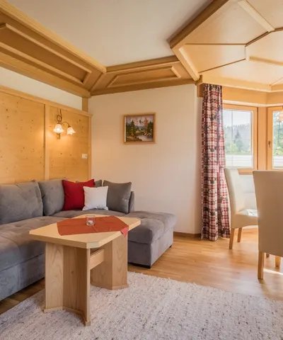 Cozy alpine-style living room with grey sofa, wooden ceiling, and bright dining area